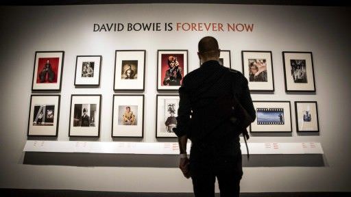 Imagen de un visitante de la exposición observando un panel con fotografías de Bowie (Fotografía: Xavier Mercadé).